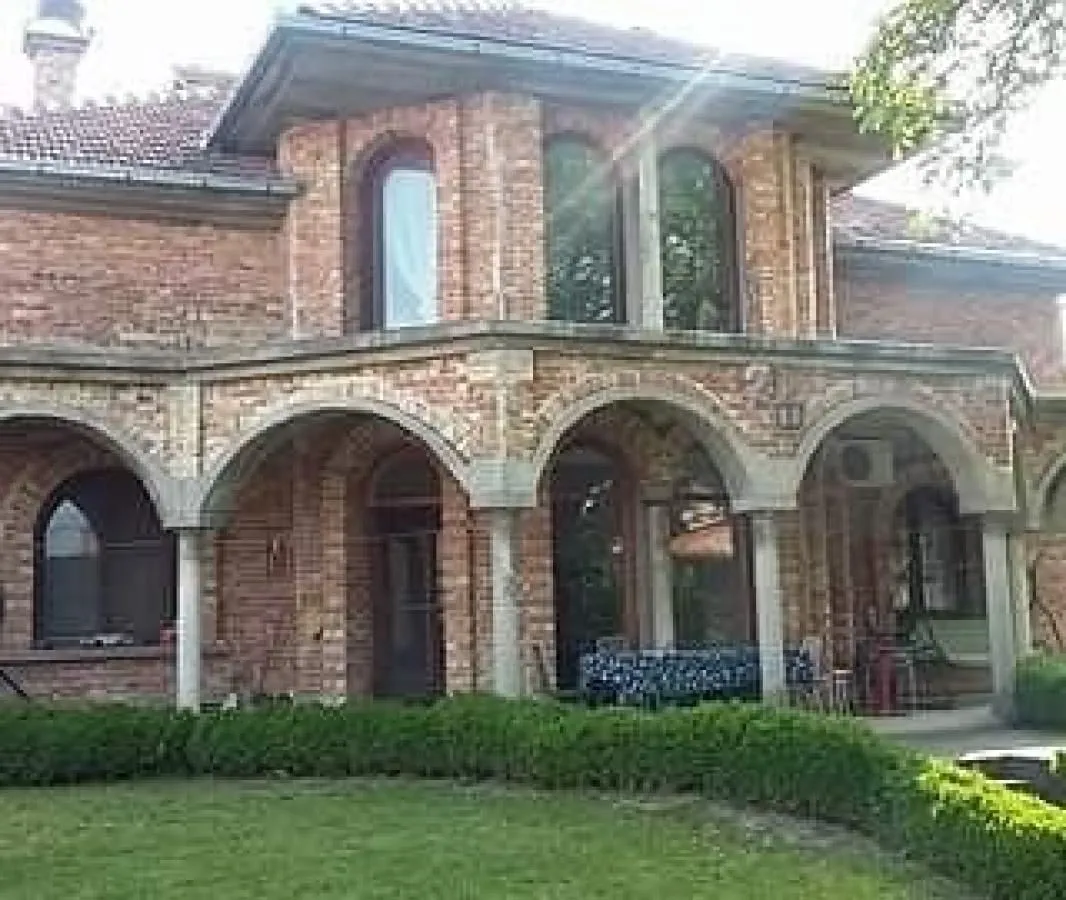 Spoljašnji izgled kuće od cigle sa lukovima i uređenim dvorištem.