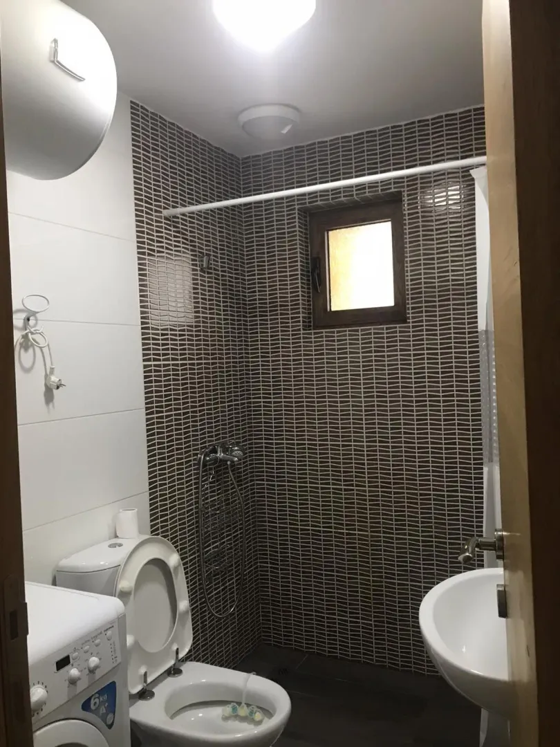Bathroom with dark tiles, a toilet, and a washing machine.