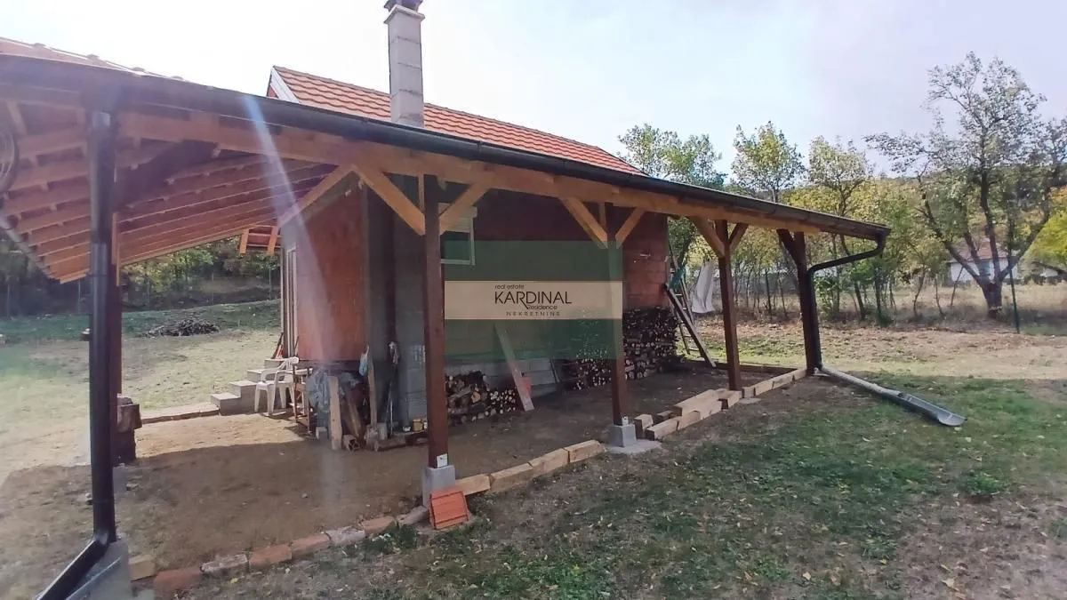 Pogled na spoljašnjost kuće sa natkrivenom drvenom terasom i dvorištem.