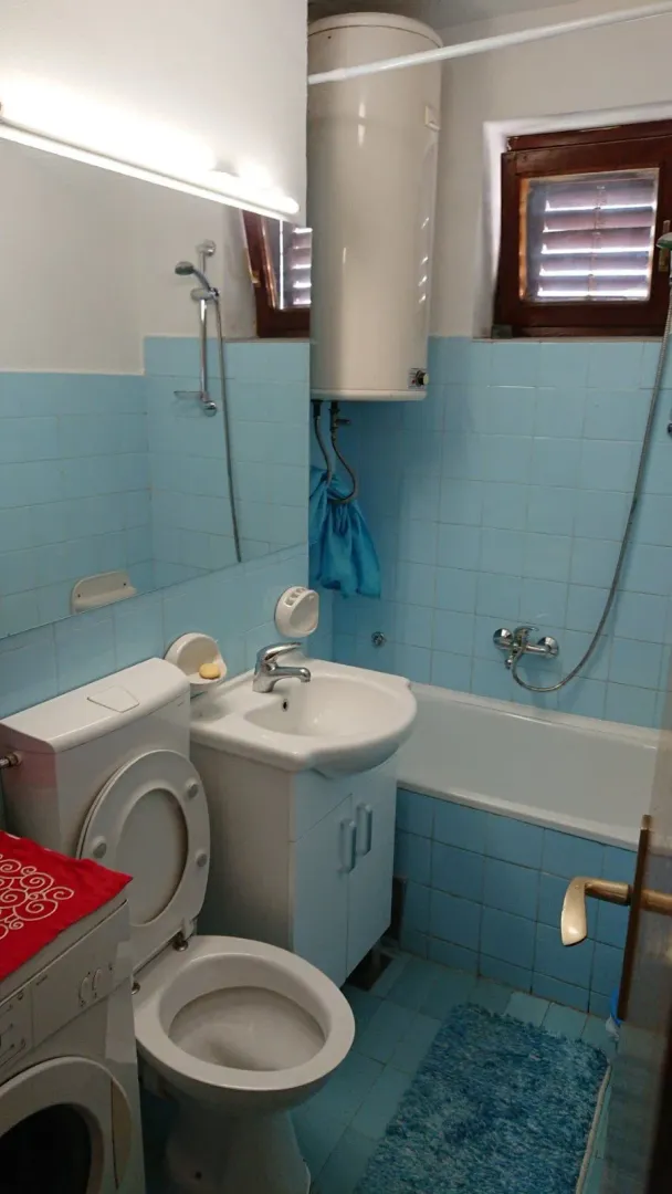 Manje kupatilo sa plavim pločicama, umivaonikom, toaletom i kadom.