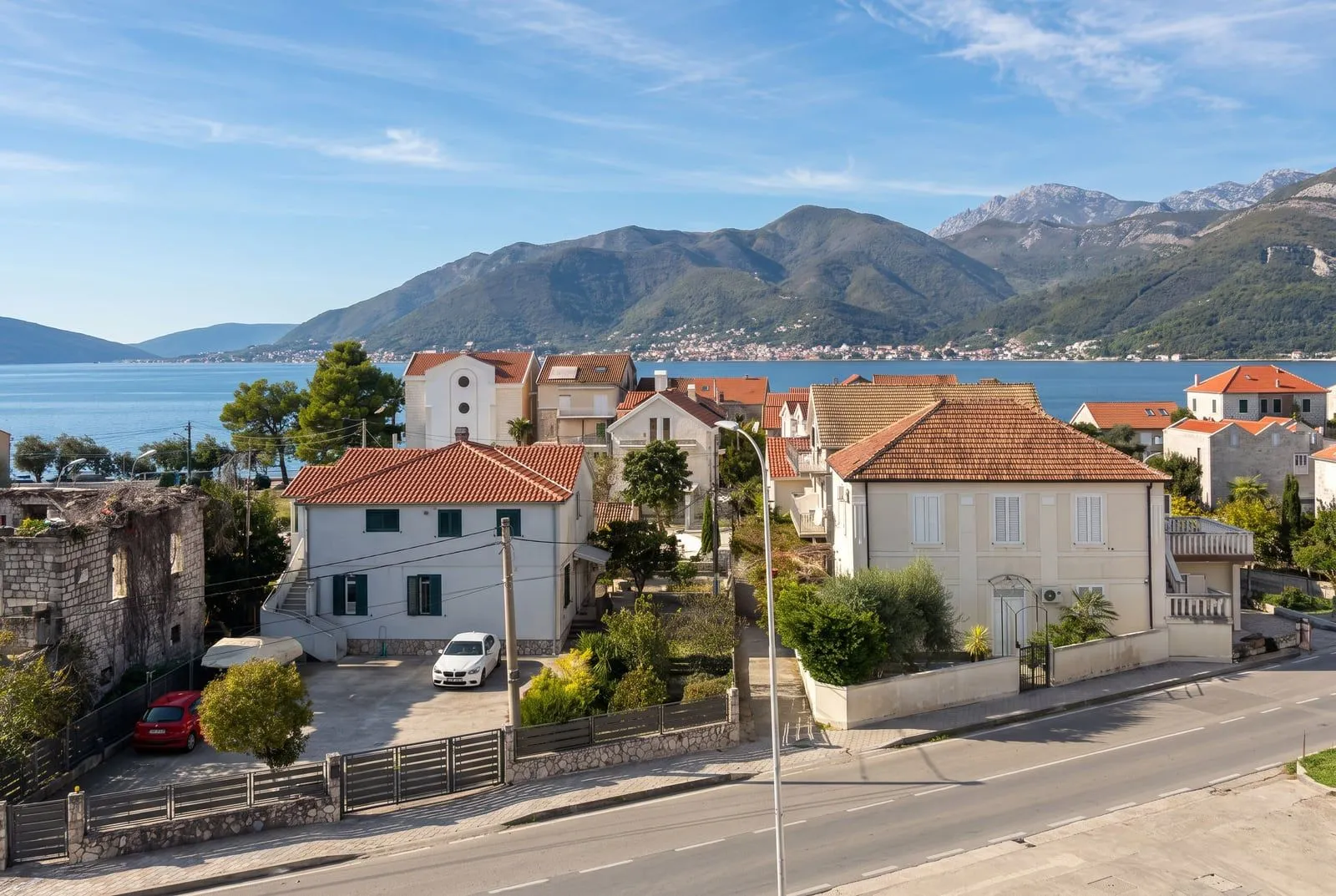 Pogled na primorske kuće sa morem i planinama u pozadini.