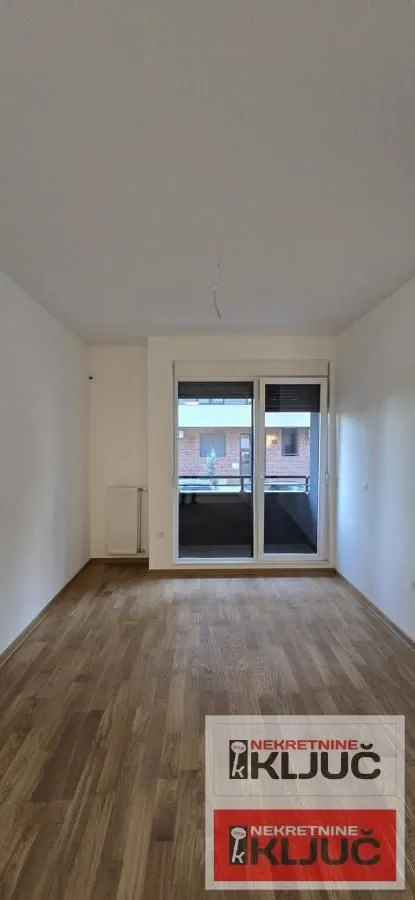 Prazna soba sa drvenim podom i izlazom na terasu.