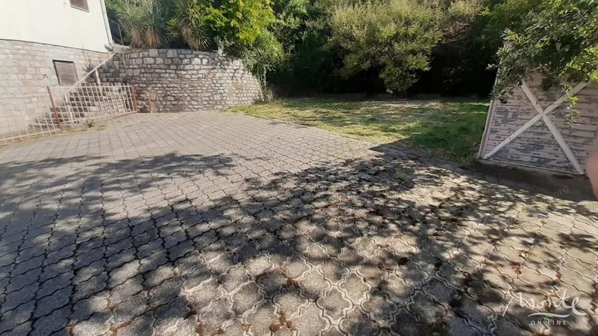 Paved yard with a green area and a stone wall in front of the house.