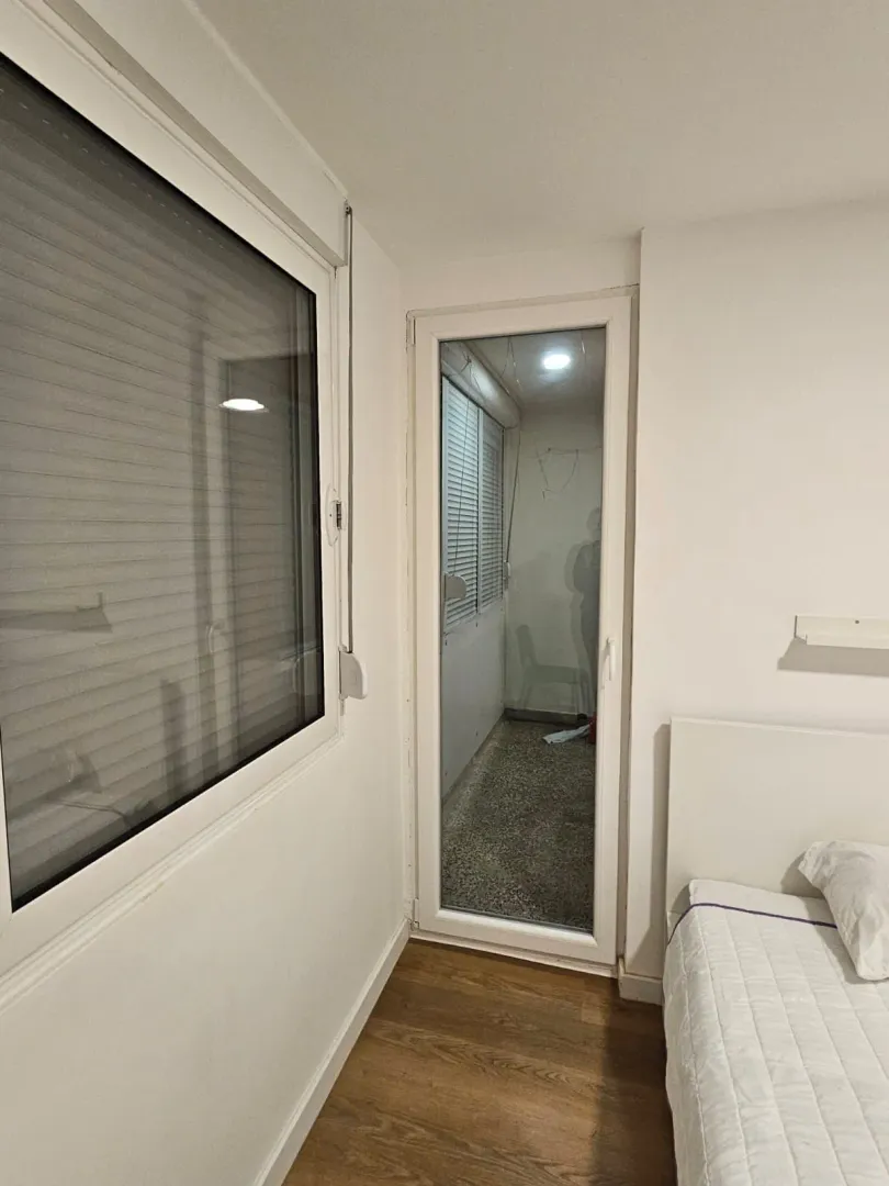 Manja spavaća soba sa krevetom i izlazom na zastakljenu terasu.