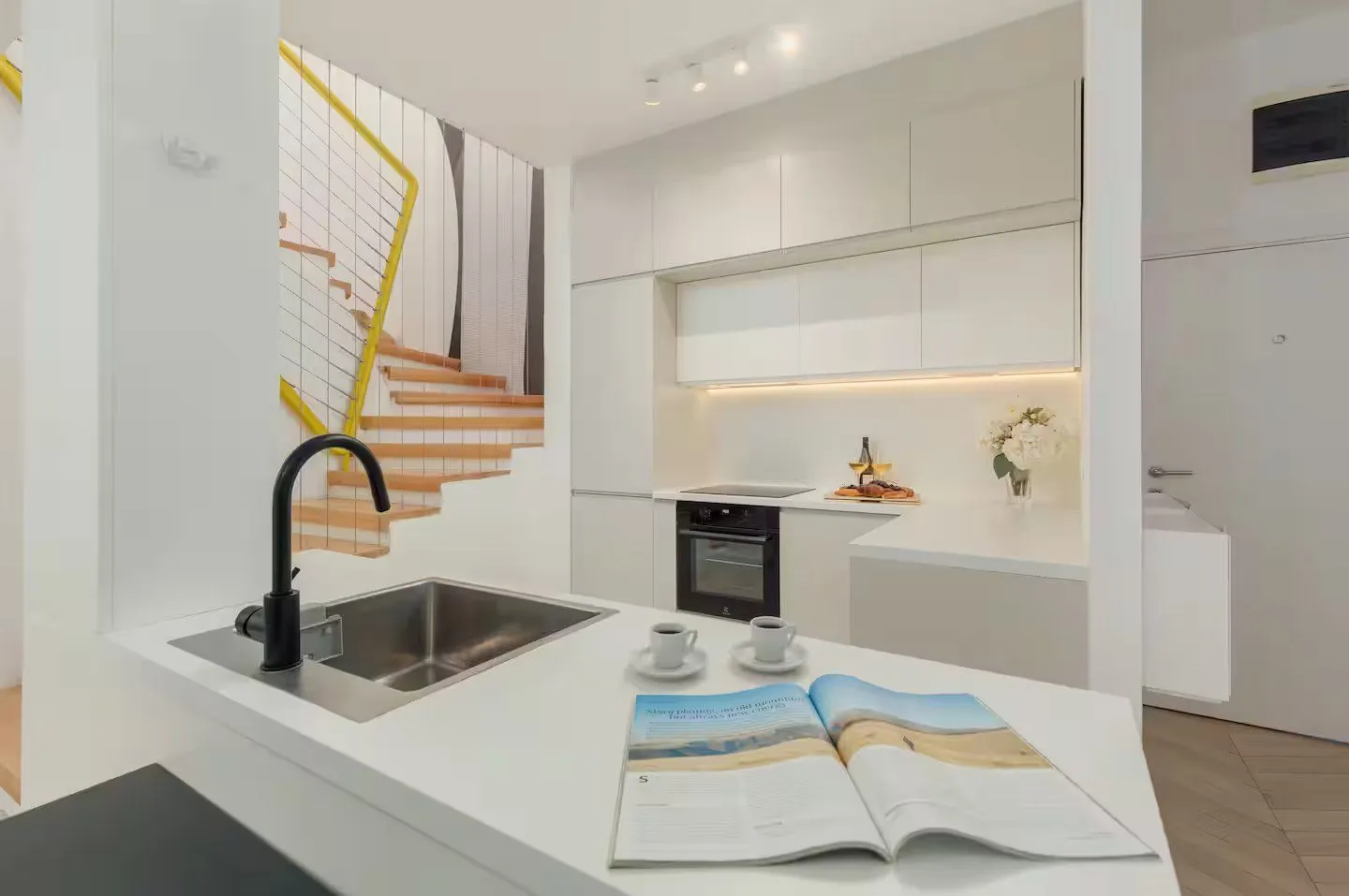 Modern white kitchen with a sink on the island and stairs in the background.