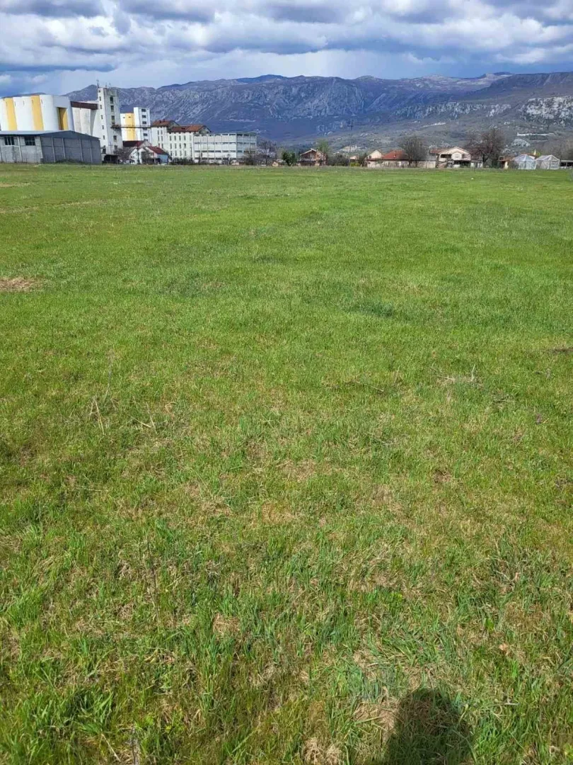 Prostran zeleni plac sa pogledom na planine u pozadini.