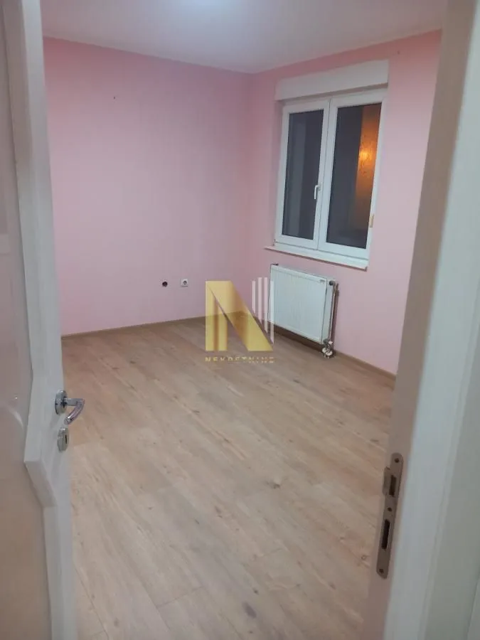 Prazna soba sa roze zidovima i drvenim podom.