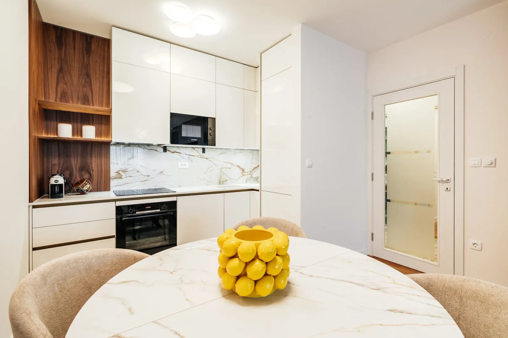 Modern kitchen with white cabinetry and a dining table in the foreground.