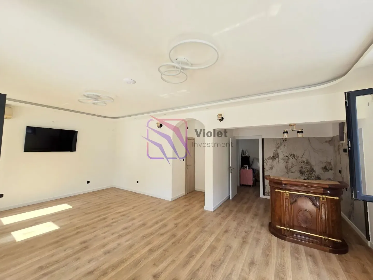Spacious empty living room with wooden flooring and a wall-mounted TV.