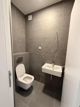 Manje kupatilo obloženo sivim pločicama sa toaletom i umivaonikom. - image 11
