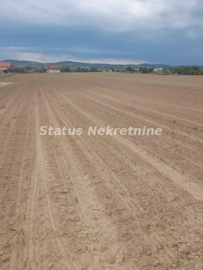 Pogled na prostrano poljoprivredno zemljište sa blagim padom i okolnim pejzažem.