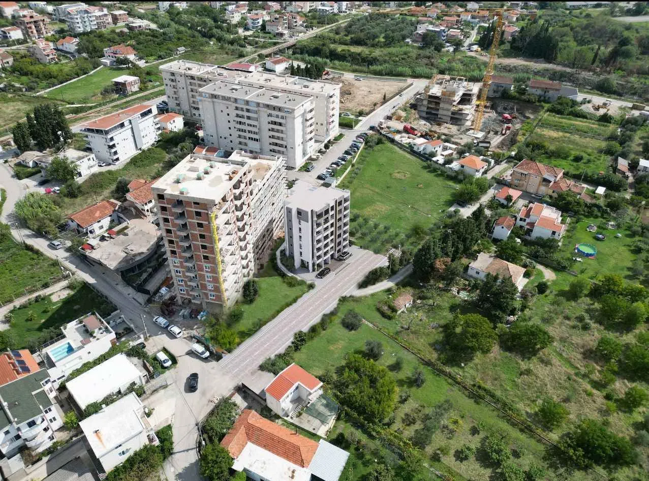 Pogled iz vazduha na stambene zgrade i okolno naselje sa zelenilom.