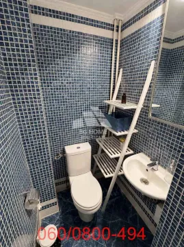 Bathroom tiled with blue mosaic tiles, featuring a toilet, a sink, and a white wooden shelf. - image 7
