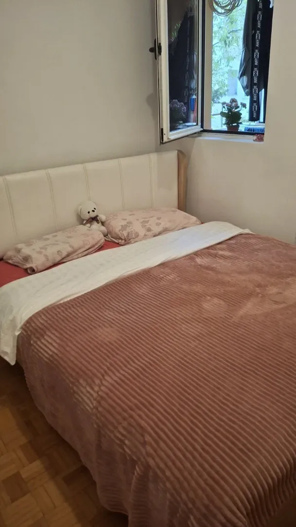 Svijetla spavaća soba sa bračnim krevetom pored otvorenog prozora.