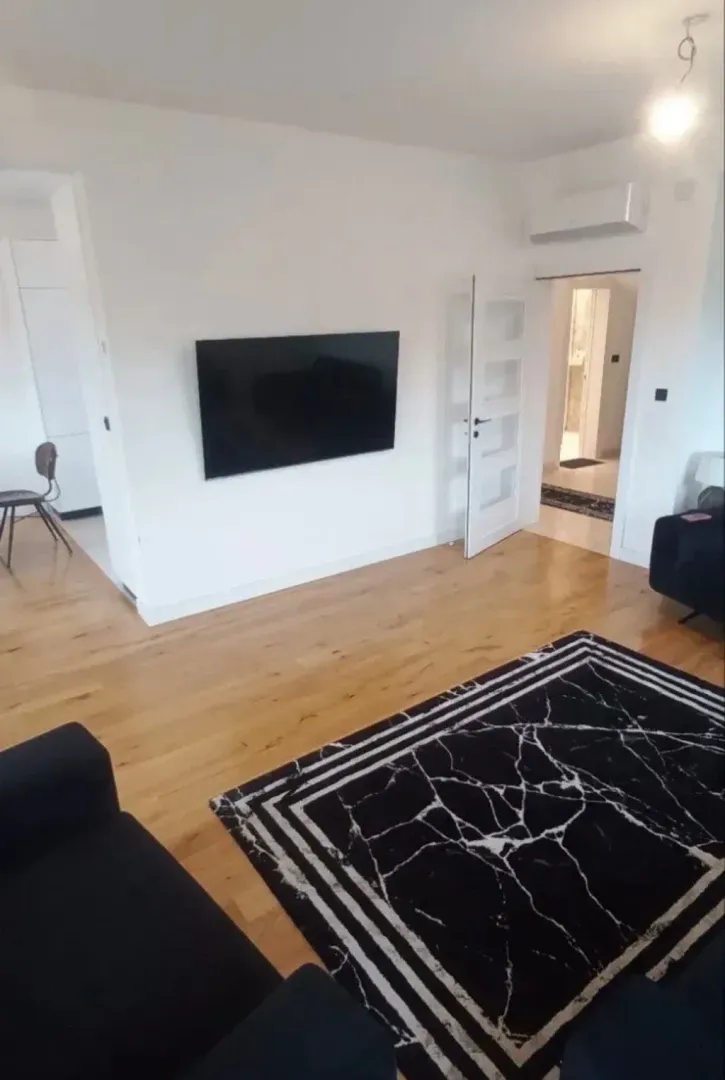 Living room with hardwood flooring, a sofa, and a wall-mounted TV.