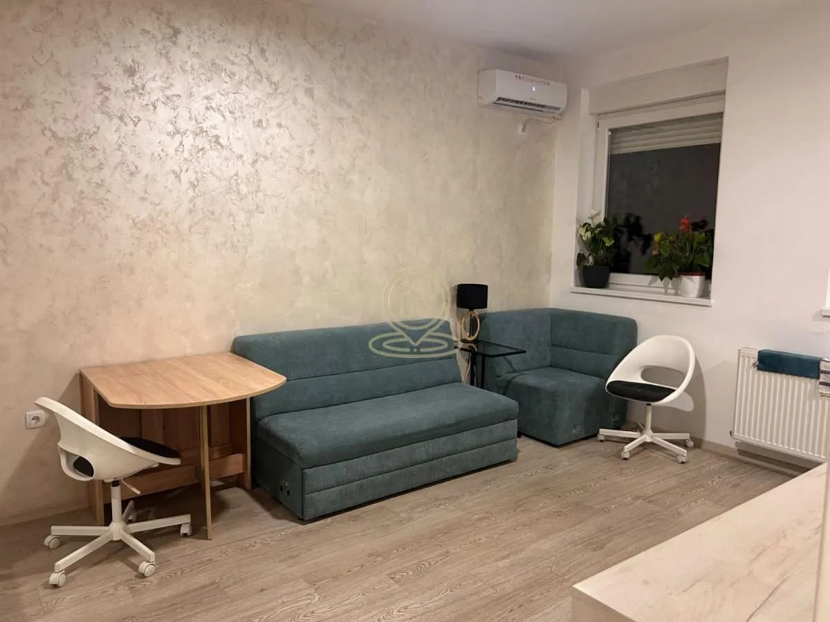 Living room with a green corner sofa, a desk, and white chairs.