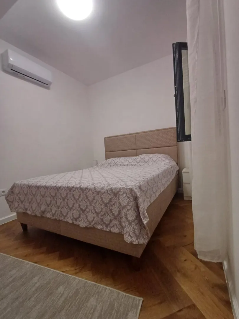 Spavaća soba sa bračnim krevetom, klima uređajem i drvenim podom.