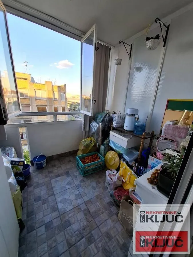 Zastakljeni balkon sa keramičkim pločicama i pogledom na okolne zgrade.