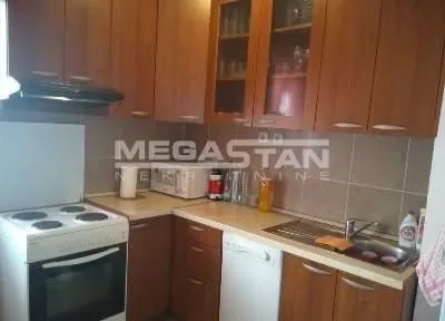 Kuhinja sa drvenim elementima, šporetom i sudoperom.