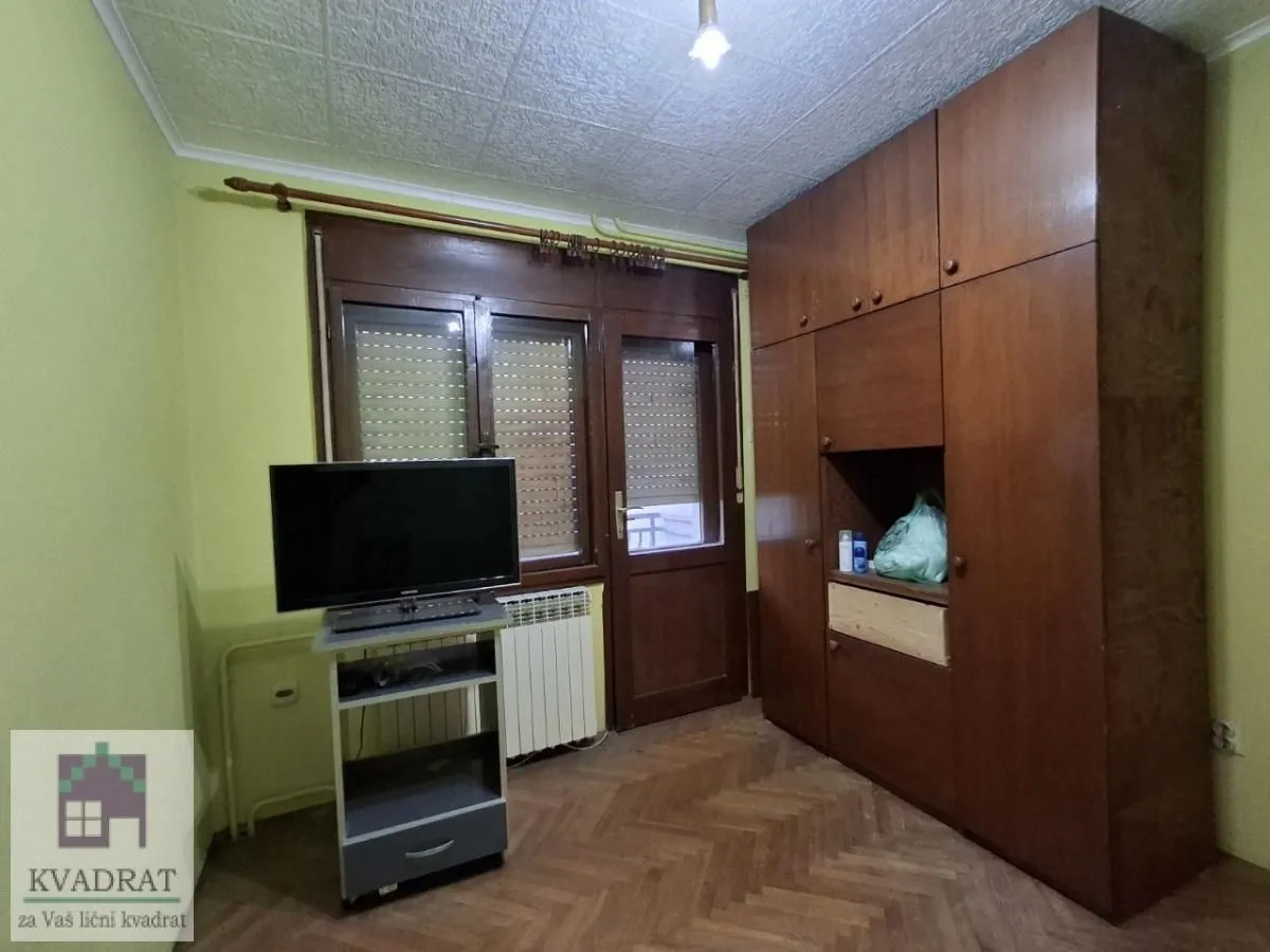 Spavaća soba sa drvenim ormanom, televizorom i parketom.