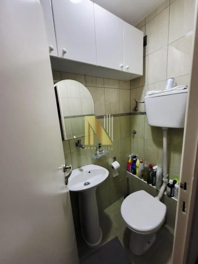 Manje kupatilo sa umivaonikom, WC šoljom i zidnim ormarićem.