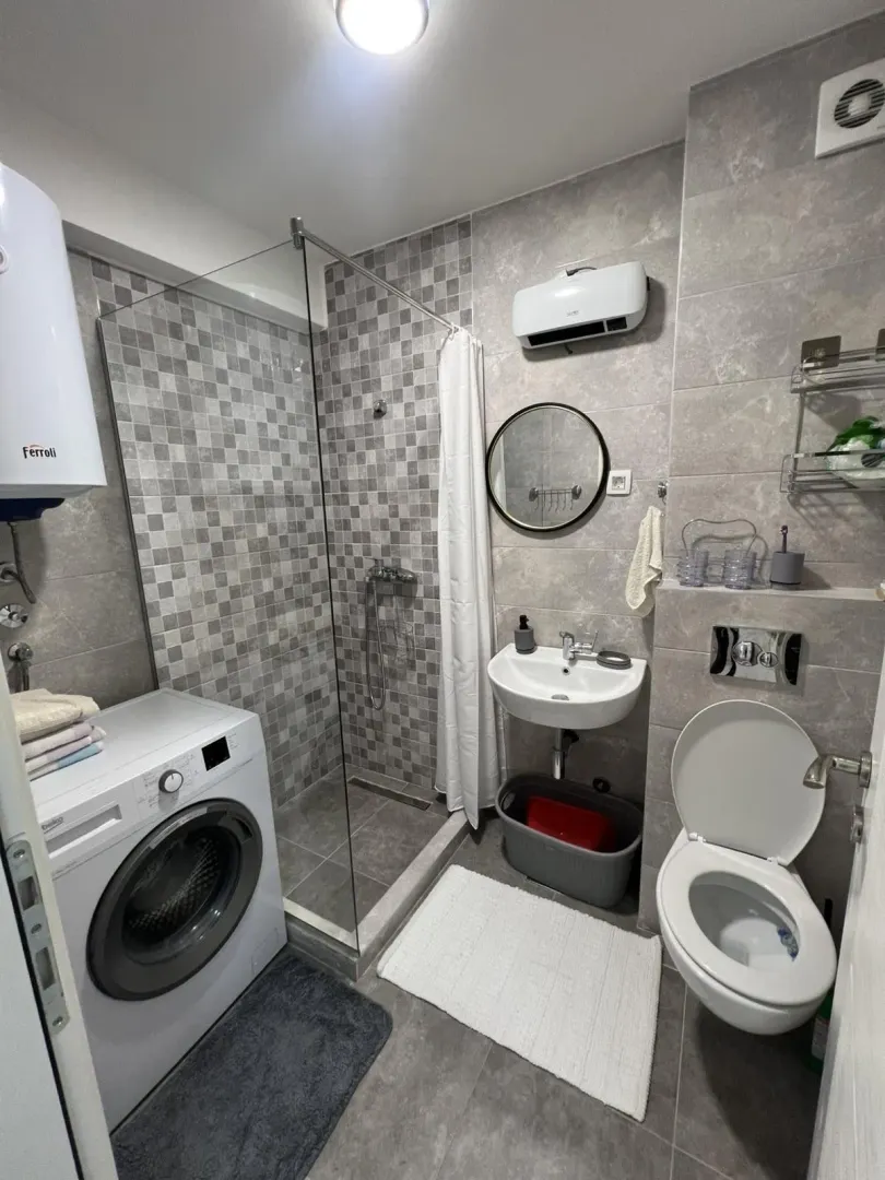 Modern bathroom with a shower cabin, washing machine, and toilet.