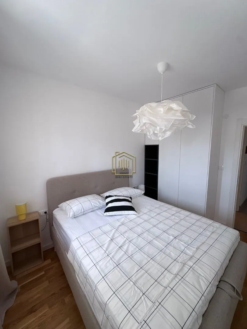 Namještena spavaća soba sa bračnim krevetom, bijelim plakarom i lusterom.