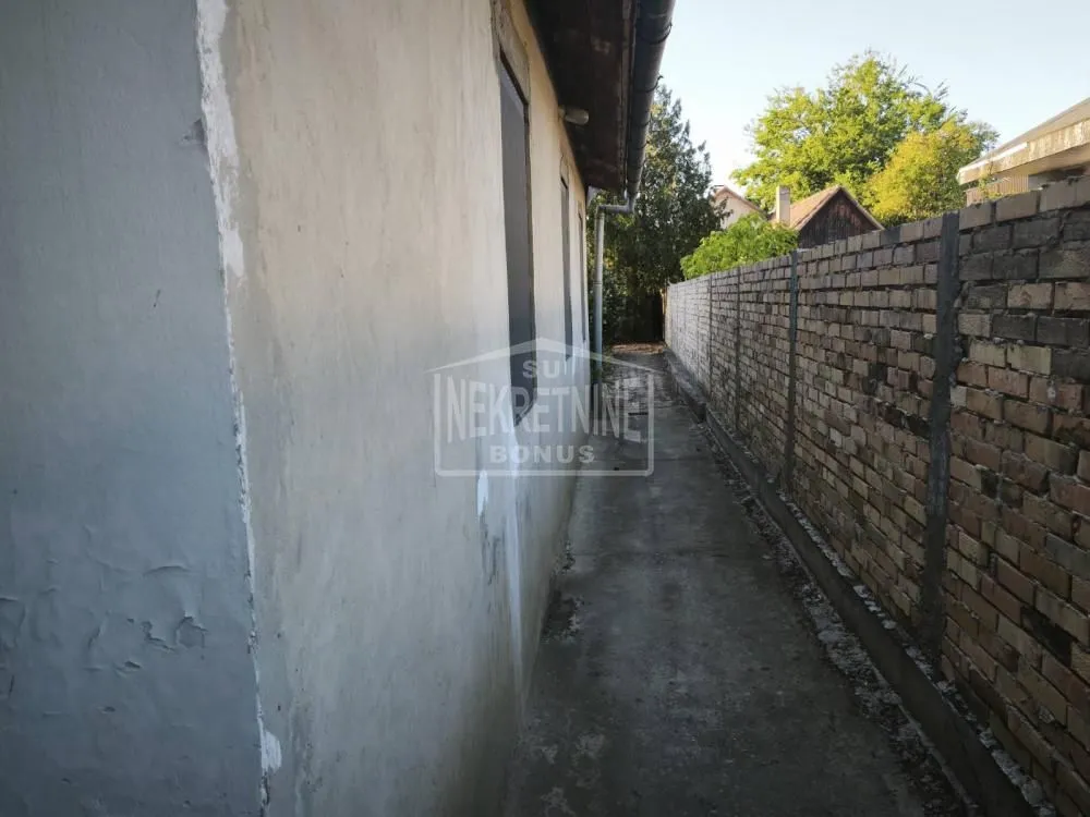 Bočni prolaz i dvorište pored kuće sa ciglenim zidom.