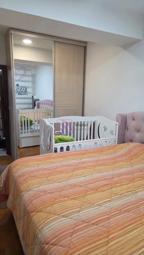 Spavaća soba sa bračnim krevetom, krevetcem za bebe i velikim ugradnim ormarom.