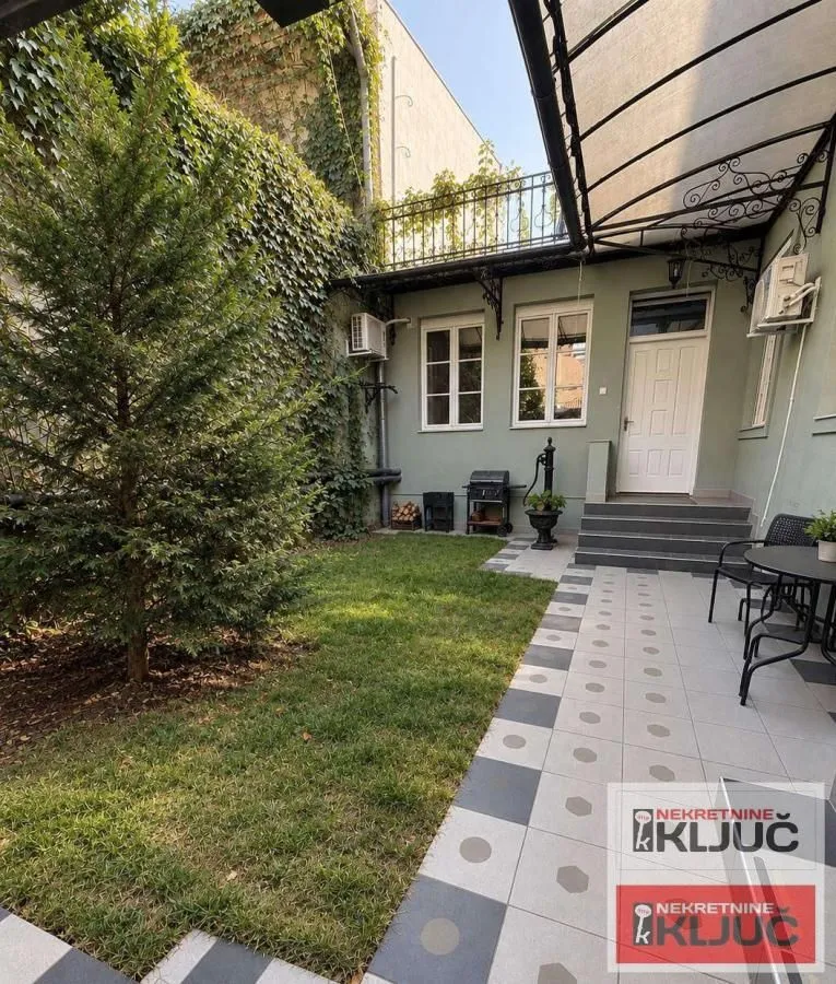 Yard with a lawn, trees, and a paved area in front of the house entrance.