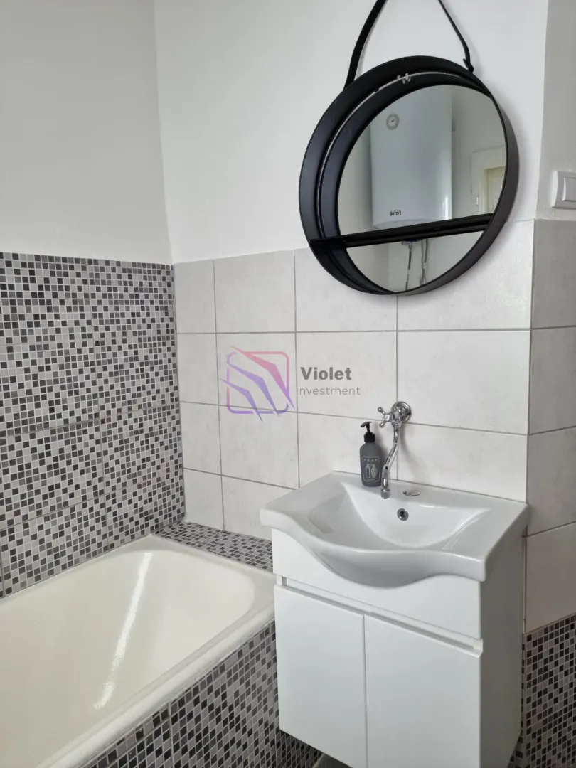 Bathroom with a sink, cabinet, round mirror, and a mosaic-tiled bathtub.