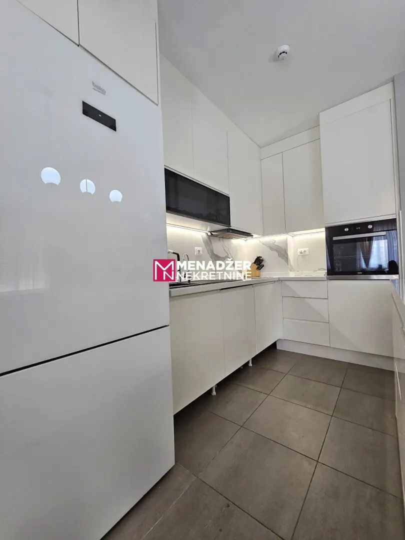 Modern white kitchen with built-in appliances and gray floor tiles.