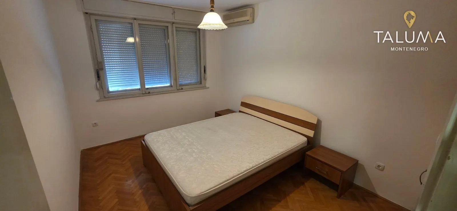 Spavaća soba sa bračnim krevetom, noćnim stočićima i parketom na podu.