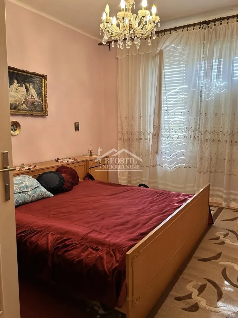 Spavaća soba sa bračnim krevetom, roze zidovima i lusterom.