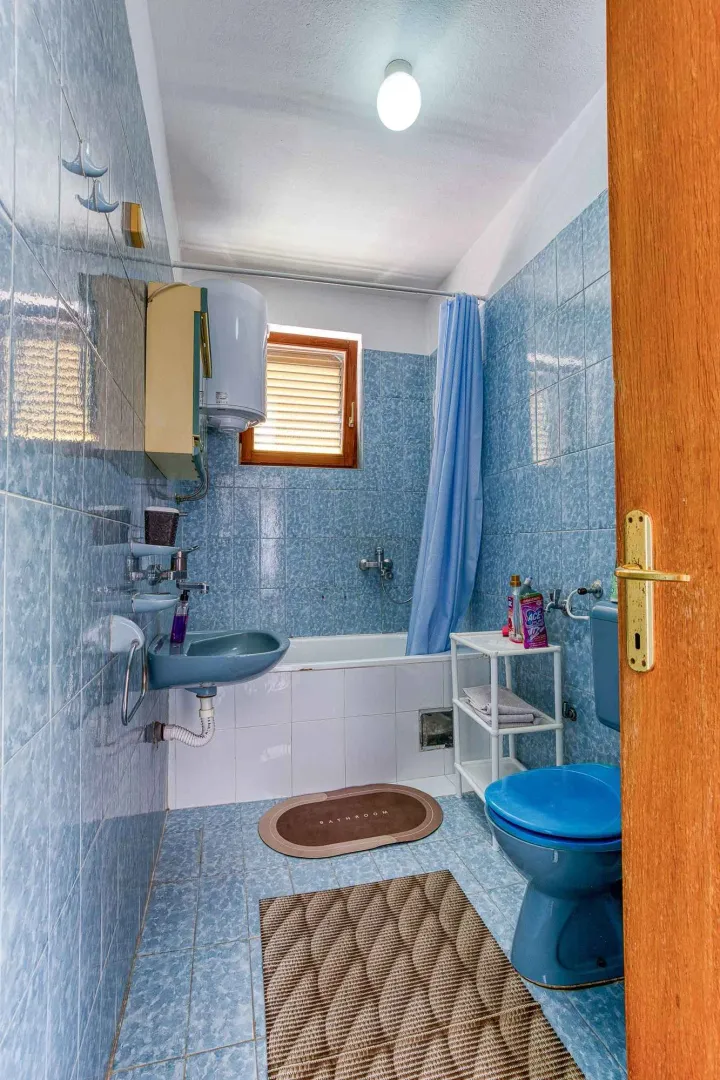 Manje kupatilo obloženo plavim pločicama sa kadom, umivaonikom i WC šoljom.