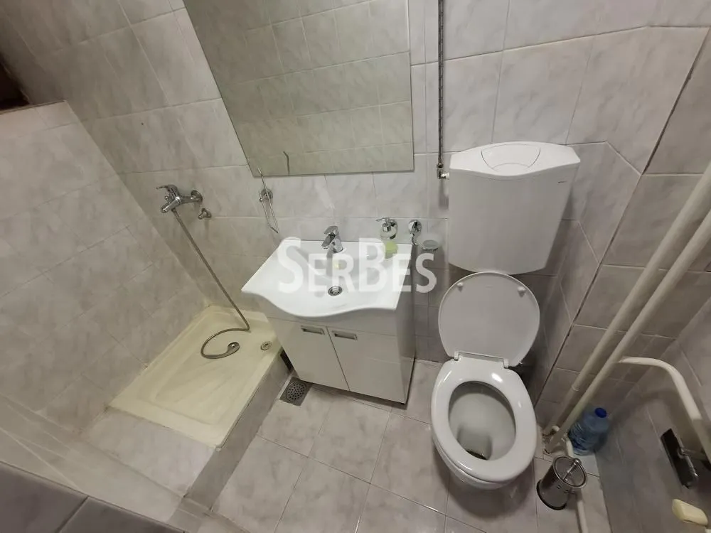 Manje kupatilo sa tuš kabinom, umivaonikom i šoljom obloženo keramičkim pločicama.