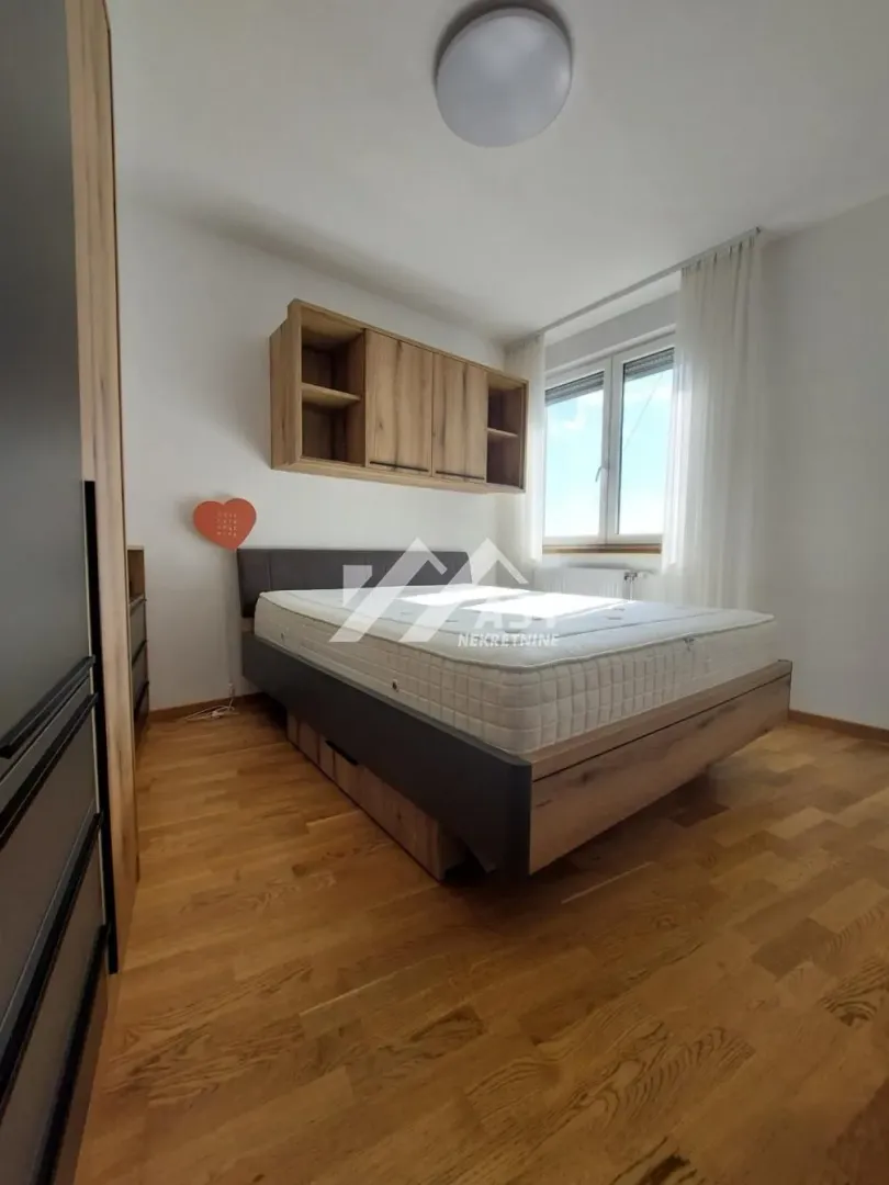 Nameštena spavaća soba sa bračnim krevetom, drvenim podom i visećim elementima.