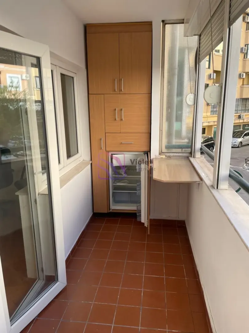 Enclosed balcony with a built-in wooden cabinet and a small refrigerator.