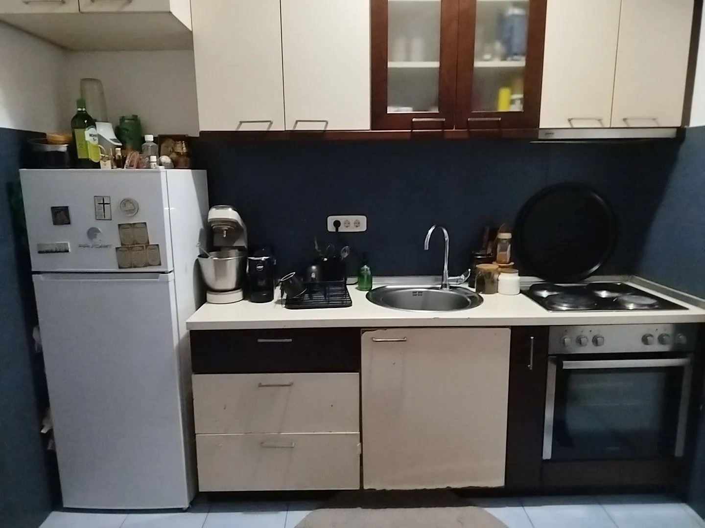 Manja kuhinja sa frižiderom, sudoperom i ugrađenom rernom.