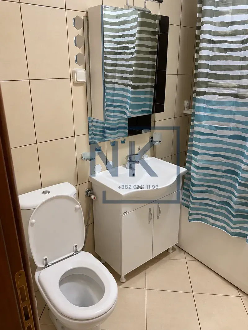 Kupatilo opremljeno umivaonikom sa ormarićem, WC šoljom i kadom sa zavjesom.
