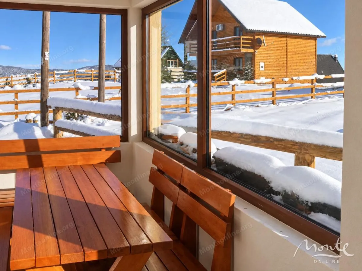 Enclosed terrace with a wooden table and benches and a view of the snow-covered landscape.