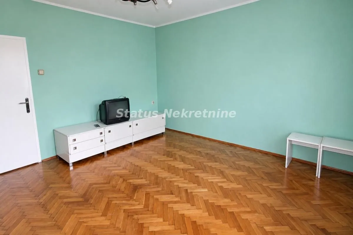 Prazna soba sa zelenim zidovima, parketom i televizorom na komodi.