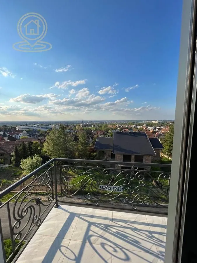 Balkon sa ukrasnom metalnom ogradom i pogledom na okolno naselje.