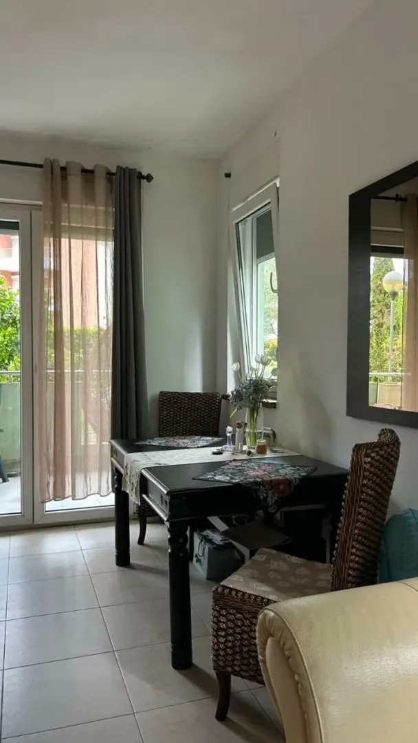 Trpezarija sa tamnim stolom i pletenim stolicama pored prozora i balkonskih vrata.
