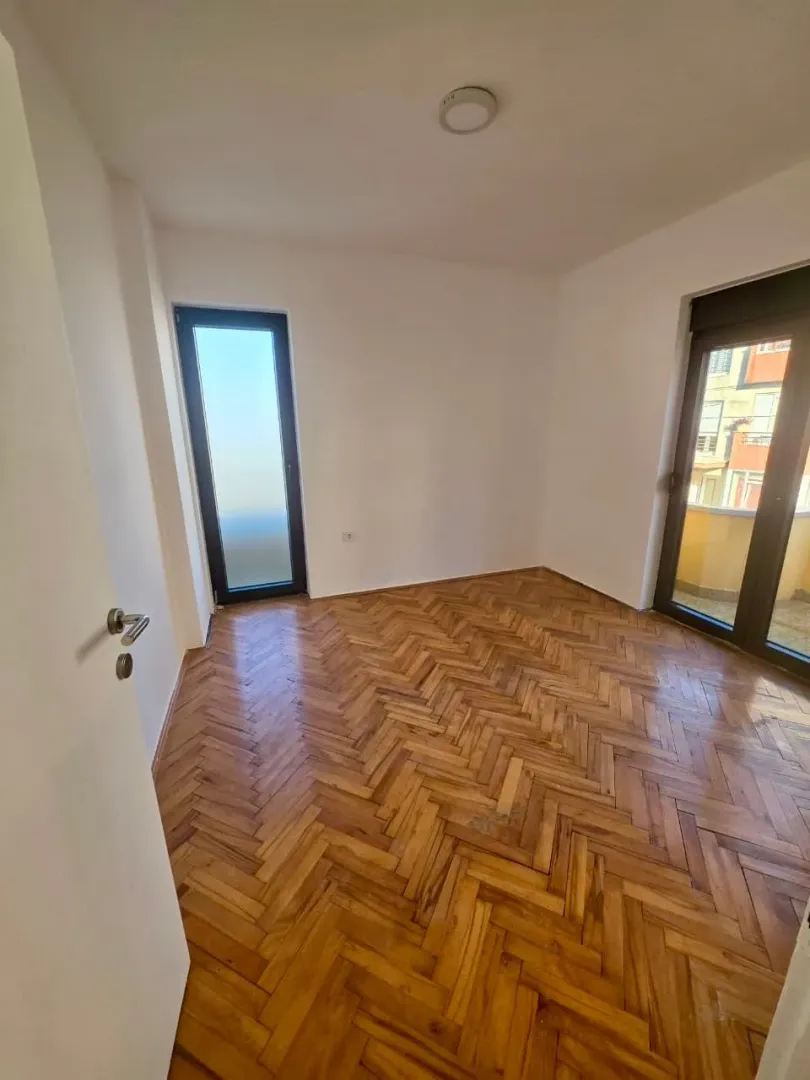 Empty room with parquet flooring and balcony doors.
