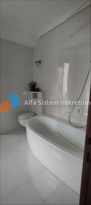 Svetlo kupatilo opremljeno kadom, tuš paravanom i toaletom.