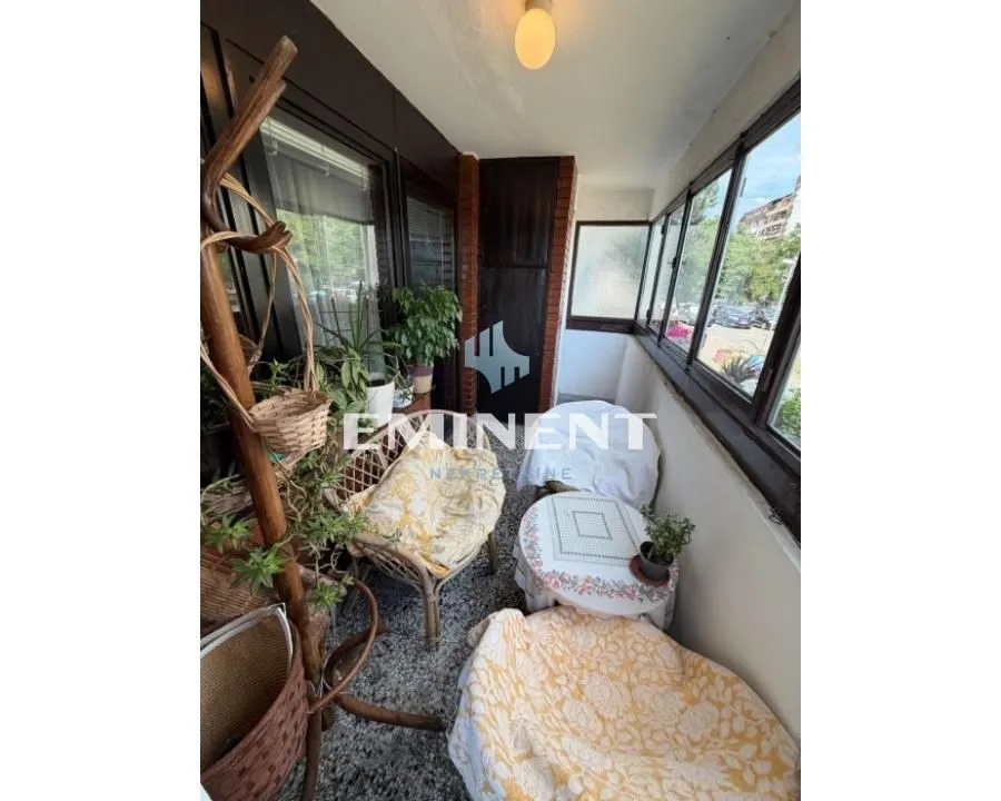 Enclosed balcony with seating furniture and plants.