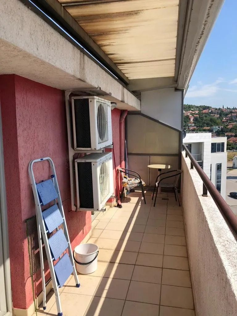 Long covered balcony with air conditioning outdoor units and seating furniture.