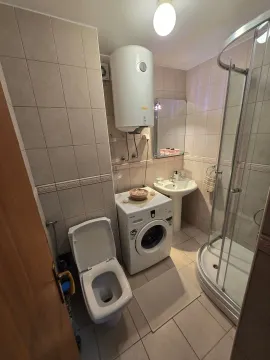 Small bathroom equipped with a shower cabin, washbasin, toilet, water heater, and washing machine. - image 5