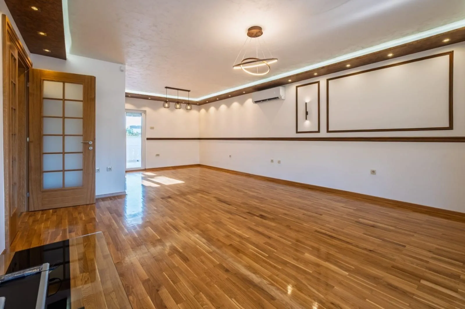 Empty living room with hardwood flooring, recessed lighting, and a door leading to the terrace.